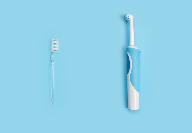 Traditional Manual and Electric Toothbrush Together Over Blue. choice between Electric toothbrushes and ordinary toothbrushes. Manual Regular Toothbrush Against Modern Electric Toothbrush