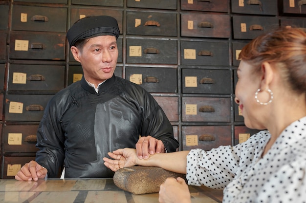 Traditional medicine practitioner checking pulse of mature woman