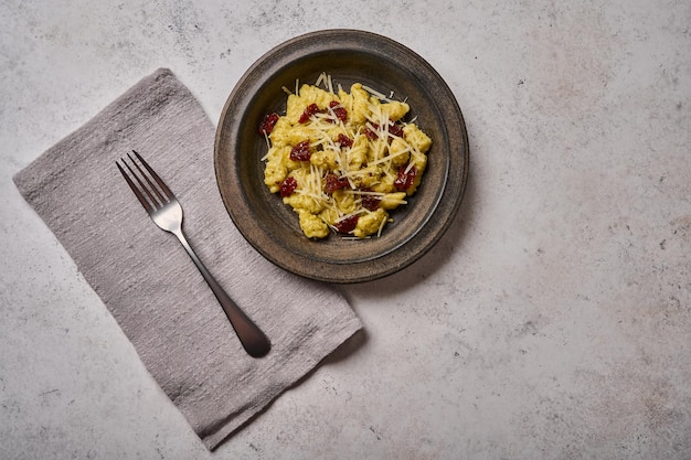 Traditional mediterranean potato gnocchi with parmesan and dried tomatoes in dark plate with fork on