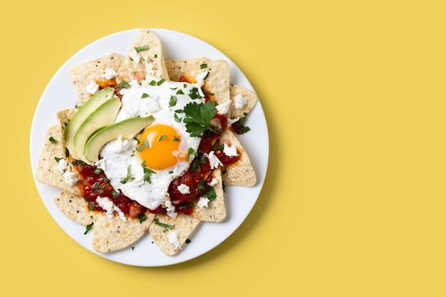 Photo traditional mexican breakfast red chilaquiles with egg on yellow background