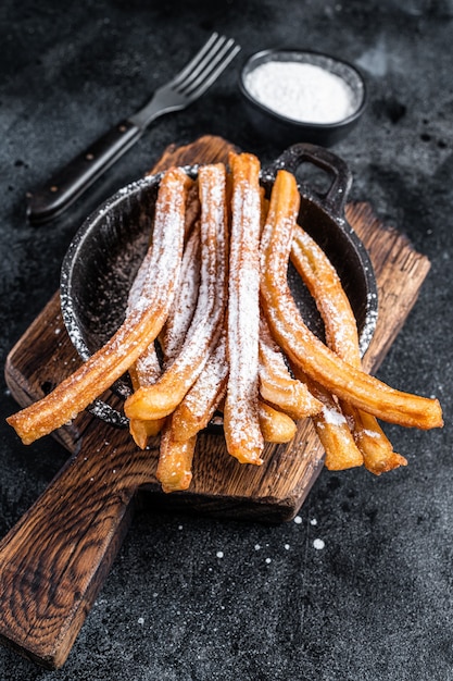 Traditional Mexican dessert churros with sugar powder in a pan. Black background. Top view.
