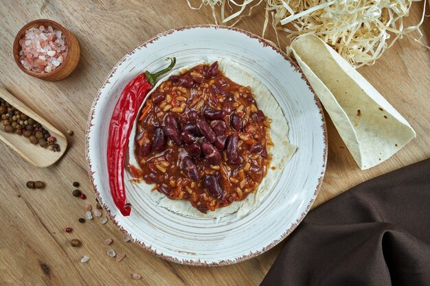 Taci messicani tradizionali con i fagioli, chili peppers in piatto ceramico bianco sulla tavola di legno. gustosi burritos di chili con carne in tacos di mais