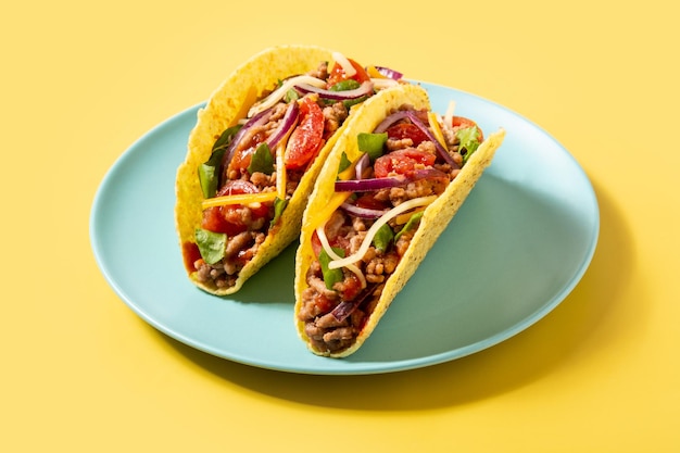 Traditional Mexican tacos with meat and vegetables on yellow background