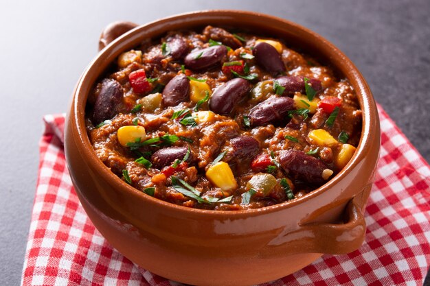 Traditional mexican tex mex chili con carne in a bowl on black background.