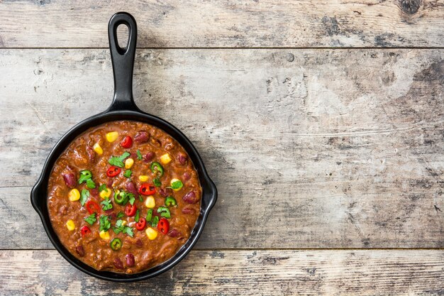 Traditional mexican tex mex chili con carne in a frying pan on wooden table flat lay