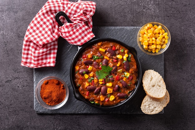 Traditional mexican tex mex chili con carne in iron pan on black stone background