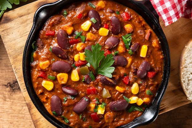 Traditional mexican tex mex chili con carne in iron pan on wooden table