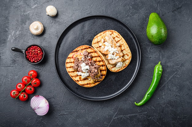 Traditional mexican tortilla with a mix of ingredients a side on black plate over black background