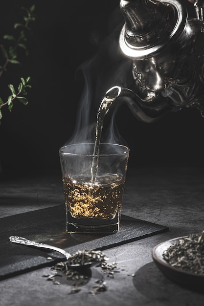 Traditional Moroccan teapot pouring tea into a steaming glass with natural tea and mint