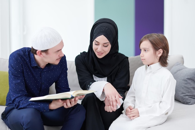 Traditional muslim family parents with children reading Quran and praying together on the sofa before iftar dinner during a ramadan feast at home