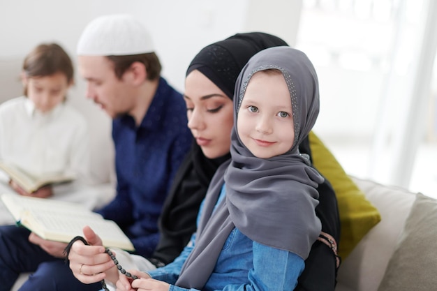 Traditional muslim family parents with children reading Quran and praying together on the sofa before iftar dinner during a ramadan feast at home