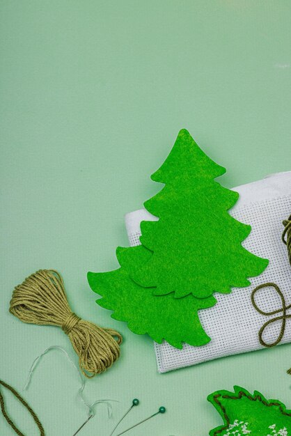 Traditional New Year compositionFestive handmade decor felt Christmas trees embroidered with a cross Holiday time concept light green background top view