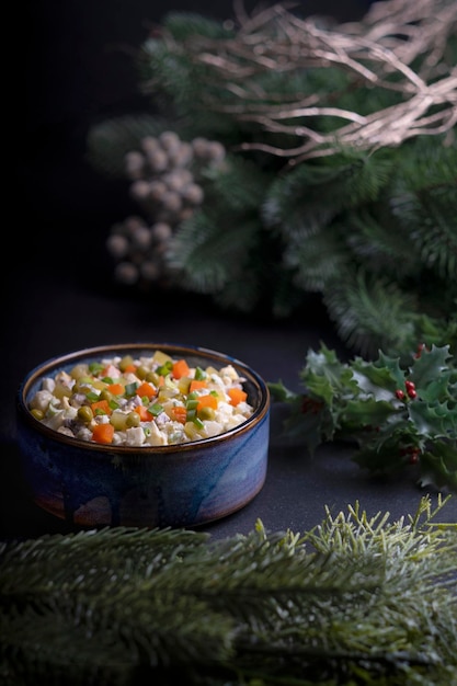 a traditional New Year's salad in a plate stands on a black background, fir branches lie nearby
