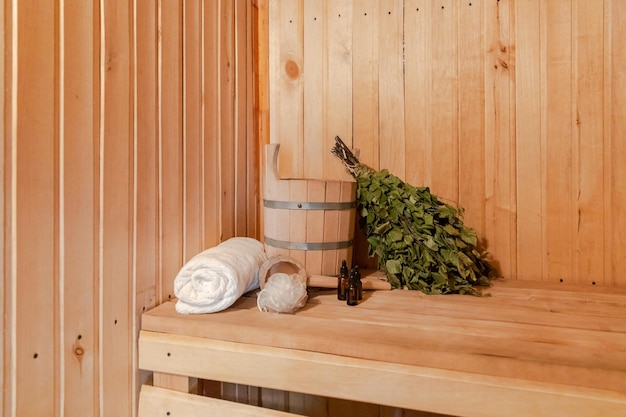 Traditional old Russian bathhouse SPA Concept. Interior details Finnish sauna steam room with traditional sauna accessories set basin birch broom towel aroma oil. Relax country village bath concept.