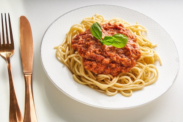 Traditional pasta bolognese served on a white plate and garnished with basil