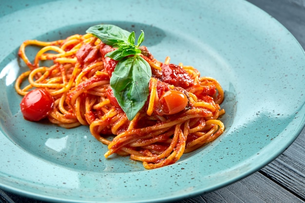 Traditional pasta spaghetti Arrabbiata sauce (with red garlic, paprika and tomato) with basil, served in a blue plate on a black, wooden surface