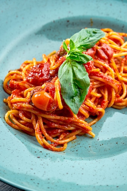 Traditional pasta spaghetti Arrabbiata sauce (with red garlic, paprika and tomato) with basil, served in a blue plate on a black, wooden surface