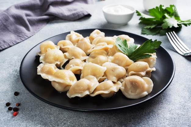 Pelmeni tradizionali, ravioli, gnocchi ripieni di carne alla piastra, cucina russa. sfondo di cemento chiaro, copia dello spazio.