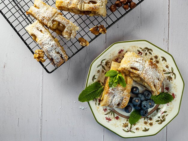 A traditional piece of apple strudel with powdered sugar mint blueberry and cinnamon in the foreground on a table Top view