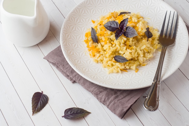 Pilaf tradizionale, riso con verdure e basilico fresco in un piatto su un tavolo di legno chiaro.