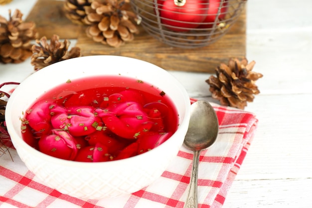 Traditional polish clear red borscht with dumplings in bowl on tray and Christmas decorations on wooden background