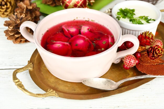 Traditional polish clear red borscht with dumplings in bowl on tray and Christmas decorations on wooden surface