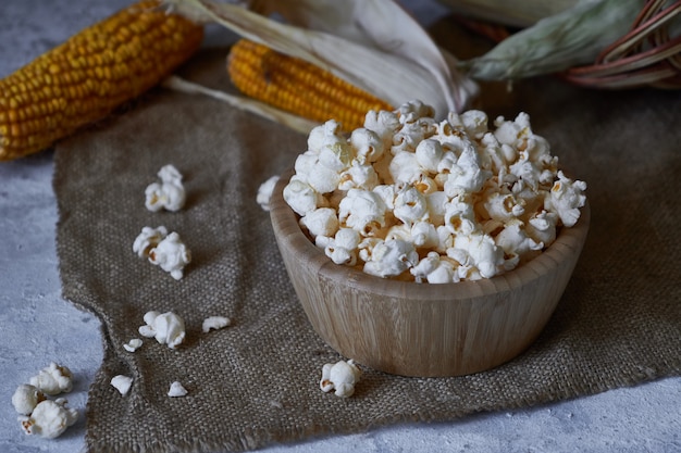 Traditional popcorn in a wooden bowl and corncobs on the table.