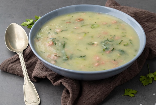 Traditional portuguese green soup with potato green cabbage and sausage in a bowl over stone background