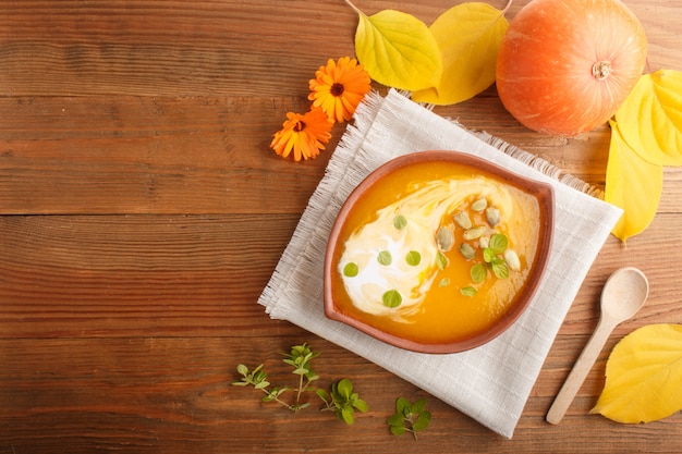 Традиционный суп из тыквы крем с семенами в глиняной миски на коричневый деревянный фон с льняной салфеткой. вид сверху.