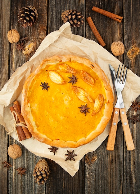 Traditional pumpkin pie on a wooden table in autumn leaves. Close-up, top view.