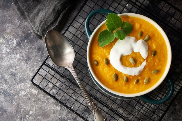 Traditional pumpkin soup puree with cream and seeds in a bowl, on a dark background