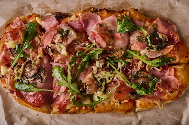 Traditional rectangular roman pizza with prosciutto ham tomatoes mozzarella mushrooms and arugula