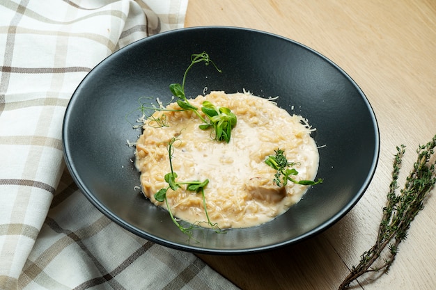 Porcini 버섯, 치즈와 나무 배경에 세련 된 검은 그릇에 마이크로 그린 전통적인 리조또.