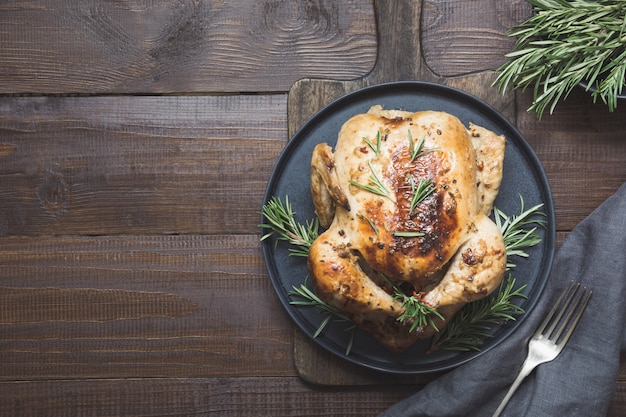 Traditional roasted chicken garnish rosemary on wooden table. Top view.