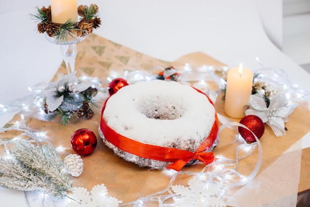 Traditional round Christmas stollen made of dried fruits and nuts sprinkled with powdered sugar on the background of a Christmas decor with candles. Traditional Christmas cupcake.