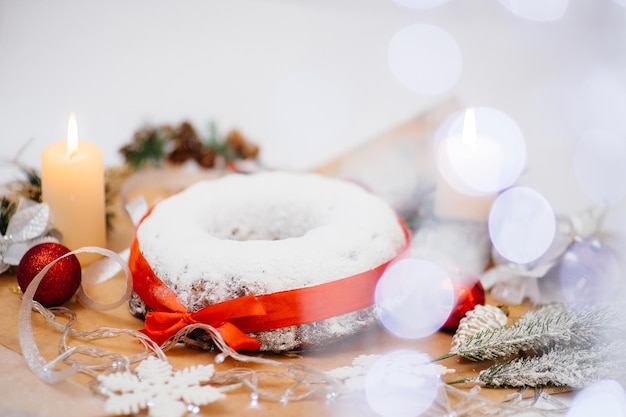 Traditional round Christmas stollen made of dried fruits and nuts sprinkled with powdered sugar on the background of a Christmas decor with candles. Traditional Christmas cupcake.