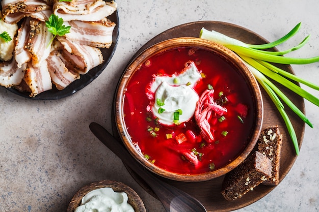 Borsch russo tradizionale con panna acida, pangrattato di segale e cipolle verdi nella ciotola di legno, vista dall'alto. concetto di cucina russa tradizionale.