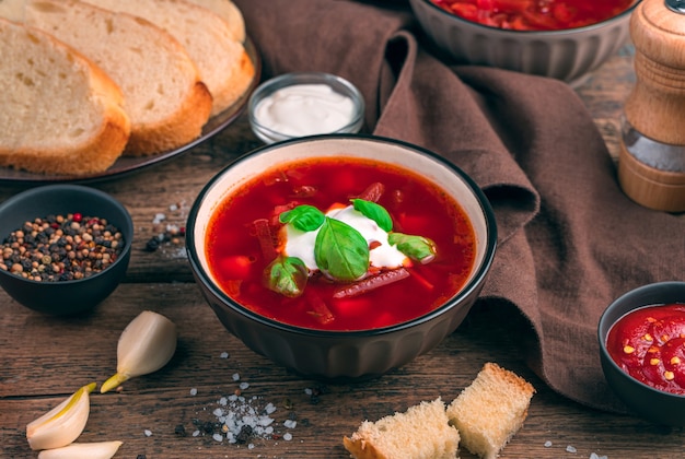 Traditional Russian borscht with beetroot on a background of garlic, bread and spice. The concept of culinary backgrounds.