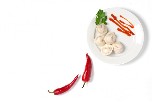 Traditional Russian dumplings, ravioli, dumplings on a white plate with red sauce and parsley. 