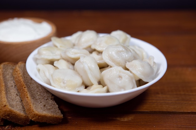 Traditional Russian dumplings with sour cream on a wooden background closeup