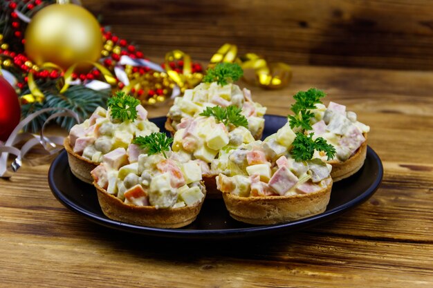 Traditional Russian festive salad Olivier in tartlets and Christmas decorations on wooden table