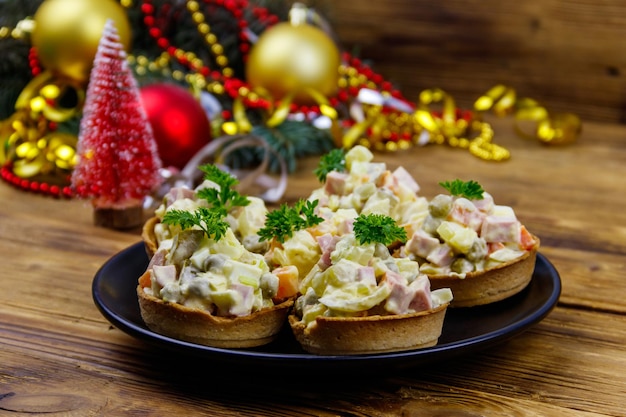 Traditional Russian festive salad Olivier in tartlets and Christmas decorations on wooden table