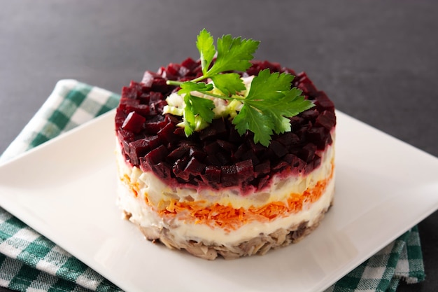 Traditional Russian herring salad with beetroot and carrots on black background