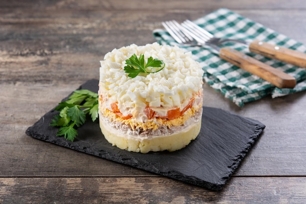 Traditional Russian layered salad Mimosa on wooden table