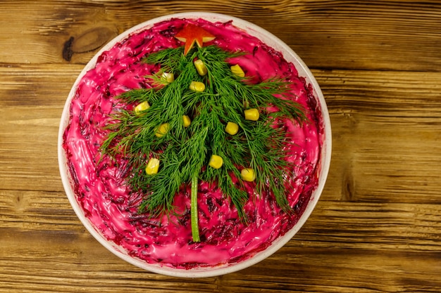 Traditional russian salad "Herring under a fur coat" (shuba) on wooden table. Salad decorated with Christmas tree made from dill and sweet corn. Top view