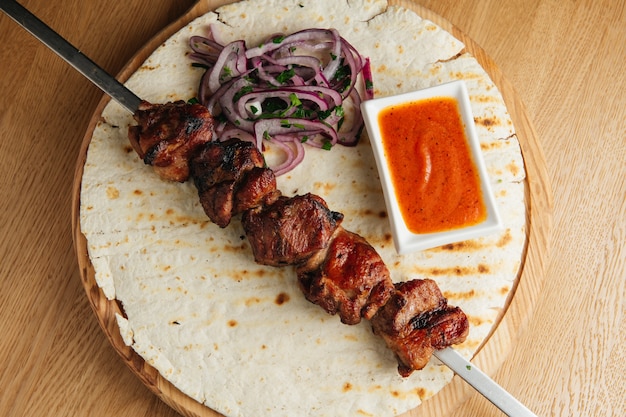 Traditional Russian shashlik on a barbecue skewer with onion, lavash and sauce on wooden board