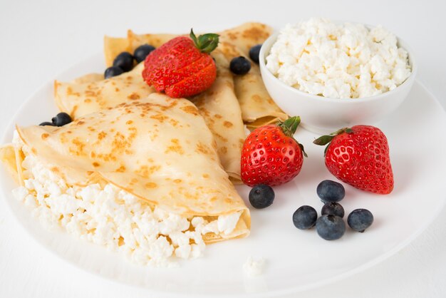 Traditional Russian thin pancakes with cottage cheese and berries in a plate on a white, close up