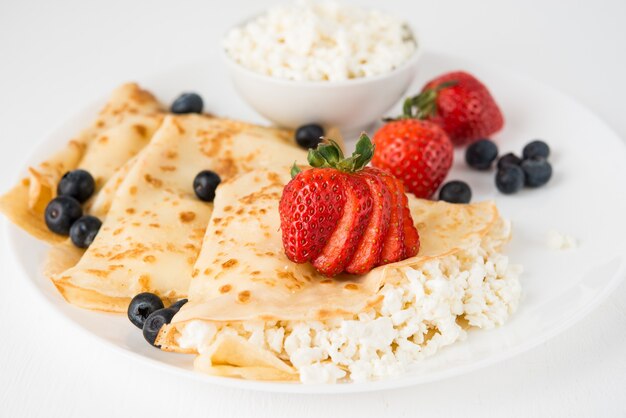 Traditional Russian thin pancakes with cottage cheese and berries in a plate on a white, selective focus