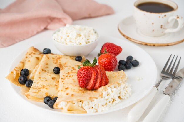 Traditional Russian thin pancakes with cottage cheese and berries in a plate on a white, selective focus