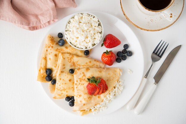 Traditional Russian thin pancakes with cottage cheese and berries in a plate on a white, top view